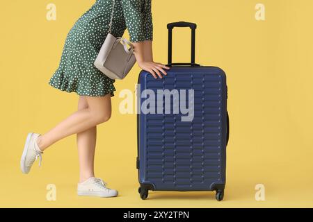 Junge Frau mit Koffer und Handtasche auf gelbem Hintergrund Stockfoto