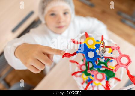 Studentin im Vorjugendalter, die auf DNA-Modell im weißen Mantel in der Schule zeigt. Ausgewählter Fokus. Hochwertige Fotos Stockfoto