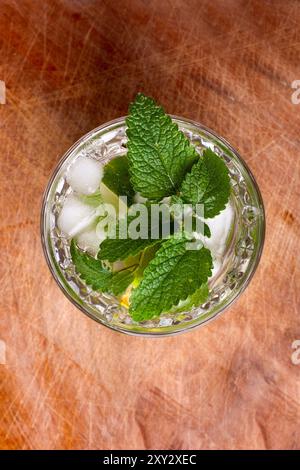 Blick von oben auf einen Mojito, der auf einem hölzernen Schneidebrett steht. Minzblätter auf dem Getränk zum Garnieren. Stockfoto