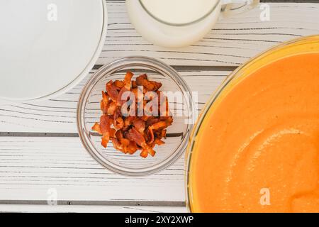 Gebratene Butternusskürbis-Suppe, serviert mit knusprigem Speck und schwerer Creme, Nahaufnahme in einer Schüssel auf einem weißen Holzbrett Stockfoto