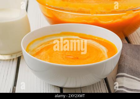 Gebratene Butternusskürbis-Suppe, serviert mit knusprigem Speck und schwerer Creme, Nahaufnahme in einer Schüssel auf einem weißen Holzbrett Stockfoto