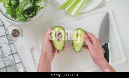 Die Hälfte der Avocado in den Händen der Frau. Rezept für grünen Salat, Zutaten auf weißem Hintergrund, flache Lay Stockfoto