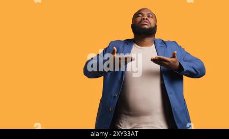 afroamerikaner ein- und ausatmen, um sich zu entspannen und positive Energie zu gewinnen, Stress zu beseitigen. BIPOC-Person, die Atemübungen für das Wohlbefinden macht, Studiohintergrund, Kamera B Stockfoto