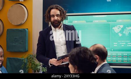 Der Projektmanager begrüßt sein Team bei einem Geschäftstreffen und schüttelt dabei die Hände. Der Vorgesetzte erläutert die allgemeinen Unternehmensziele, analysiert die aktuelle Situation und arbeitet die Planungsdetails durch. Kamera A.. Stockfoto