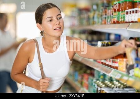 Im Supermarkt wählt die Frau ein Glas mit Konserven Stockfoto