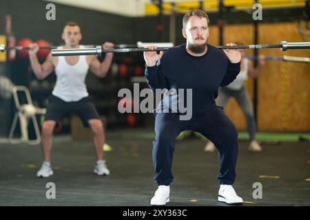 Junger bärtiger Mann, der Squats mit Langhantelstange beim intensiven Training macht Stockfoto