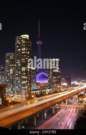 Eine beleuchtete Skyline von Toronto bei Nacht mit dem CN Tower, Rogers Centre und Lichtwegen auf einer befahrenen Autobahn im Vordergrund. Stockfoto