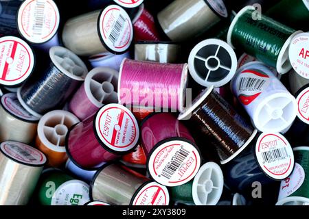 Nahaufnahme verschiedener farbenfroher Garnspulen, darunter Rosa-, Grün-, Schwarz- und Weißtöne, die in einem zufälligen Stapel angeordnet sind. Stockfoto