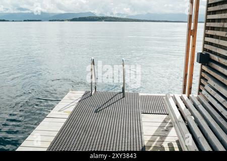 Norwegische schwimmende Sauna im skandinavischen Minimalismus mit Holzterrasse über dem ruhigen Wasser des Molde Fjords. Die Szene strahlt Ruhe aus Stockfoto