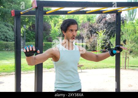 Ein Mann hält zwei rote Seile und trägt ein grünes Tanktop. Er ist in einem Park und er übt Sport Stockfoto