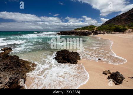 Ein sonniger Tag mit wenigen Wolken am abgelegenen und unberührten Hawaiian Monk Seal Beach im Ka’ena Point Beach Park in Oahu, mit Wellen, die sich bis zum Strand erstrecken Stockfoto