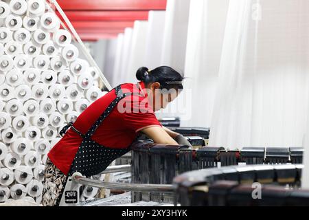 SUQIAN, CHINA - 27. AUGUST 2024 - Ein Arbeiter stellt in einer Werkstatt in Suqian, Jiangs, Kunststoffgewebe für den Export in südostasiatische Länder her Stockfoto