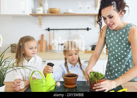 Schöne junge Frauen mit zwei kleinen niedlichen Töchter Blume Pflanzen im Topf auf der Küche Stockfoto