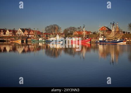 Der frühe Morgen im Hafen von Greetsiel zeigt farbenfrohe Fischerboote und ihre klaren Reflexionen im ruhigen Wasser, Greetsiel, Krummhoern, Osten Stockfoto