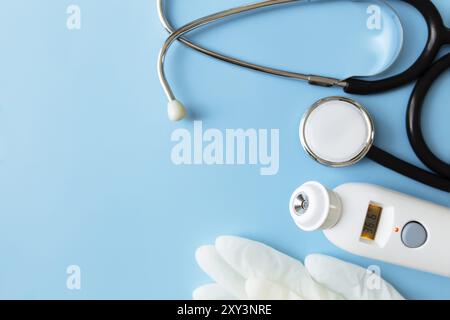 Medikamentöse Behandlungskonzepte. Elektronisches Thermometer, Phonendoskop oder Stethoskop, weiße Handschuhe auf blauem Hintergrund. Stockfoto