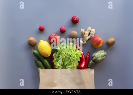 Gesundes und organisches Lebensmittelflay Lay-Konzept auf grauem Hintergrund. Öko Beutel mit verstreuten Salatblättern, Äpfeln, Kiwi, Rettich, Zitrone, Gurke, Arti Stockfoto