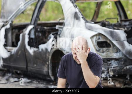 Weinender, verärgerter kaukasier bei einem Verkehrsunfall oder Brandstiftung Feuer verbrannten Rad Auto Auto-Trödel Stockfoto