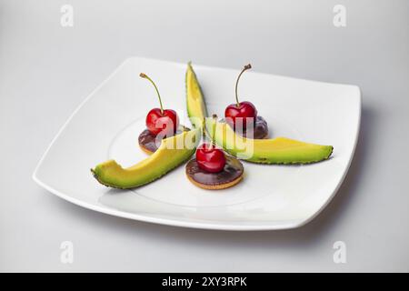 Drei Kirschen auf drei Schokoladenkeksen mit Avocadoscheiben Stockfoto