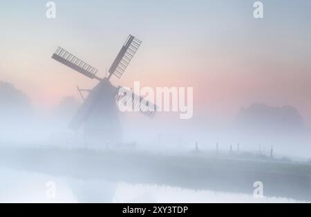 Holländische Windmühle im dichten Nebel bei Sonnenaufgang Sommer Stockfoto