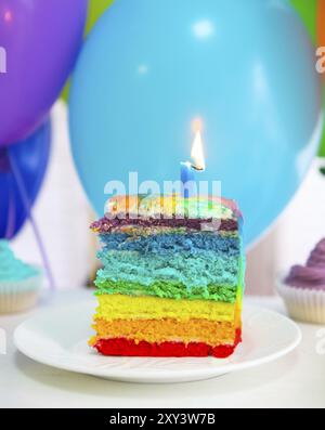 Regenbogen Kuchen verziert mit Geburtstag Kerze. Luftballons auf dem Hintergrund Stockfoto