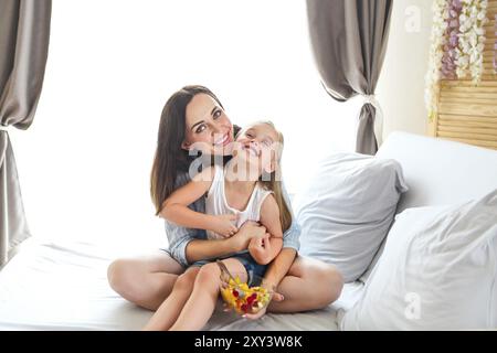 Mutter und Tochter mit Arm um auf dem Bett zu Hause sitzen in Obstsalat zum Frühstück Stockfoto