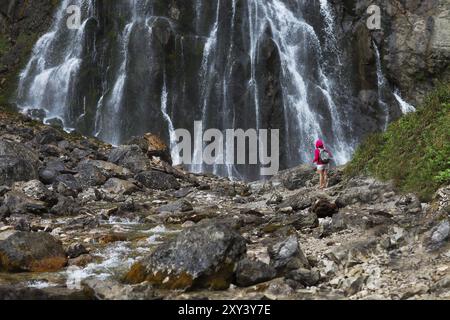 Junge hübsche touristische Mädchen mit Rucksack in der Nähe von Wasserfall in den Bergen Stockfoto