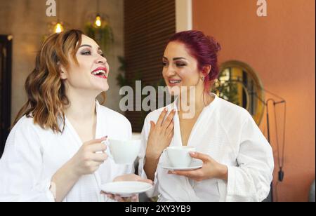 Zwei Frauen in weißen Gewändern Tee trinken nach Spa Behandlungen und Reden Stockfoto