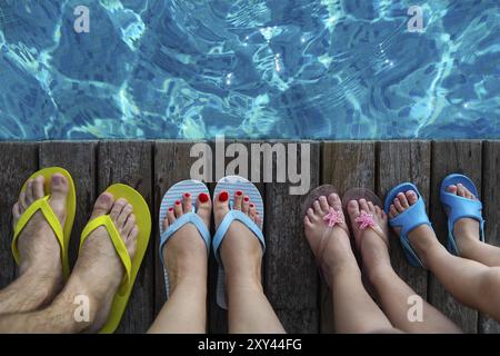 Familie tragen bunte Flip-flops auf hölzernen Hintergrund in der Nähe des Pools. Sommer Reisen und Urlaub-Konzept Stockfoto