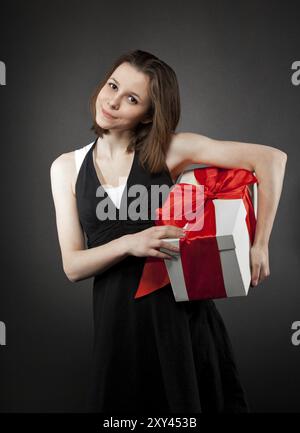 Glückliches junge Brünette Mädchen mit Geschenk dekoriert mit rotem Band Stockfoto