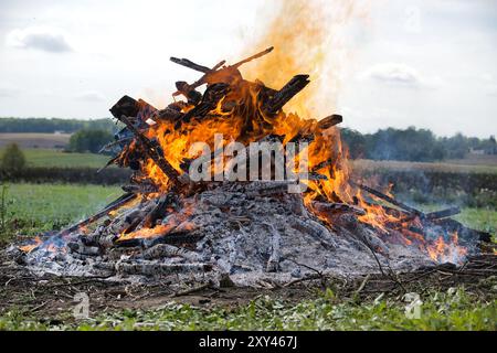 Aus nächster Nähe sehen Sie ein Lagerfeuer mit brennendem Holz, das intensive Flammen und verkohlte Baumstämme in einer Umgebung im Freien zeigt. Es fängt einen warmen, dramatischen geldautomaten ein Stockfoto