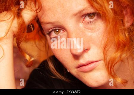 Nahaufnahme einer jungen Frau mit rotem Haar, Tränen in den Augen und einem zutiefst traurigen Ausdruck, der einen Moment emotionaler Verletzlichkeit und Trauer festhält Stockfoto