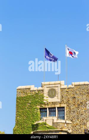 Die lila Flagge der Yonsei-Universität und die koreanische Nationalflagge Taegukgi fliegen über einem mit Efeu bedeckten Backsteinturm an einem klaren, blauen Himmel auf dem Sinchon Campus Stockfoto
