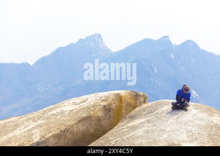 Seoul, Südkorea, 23. April 2015: Ein koreanischer Mann, der in farbenfroher Trekking-Mode auf dem Boulder auf dem Baegundae Peak liegt, nachdem er Bukhansan gewandert hat Stockfoto