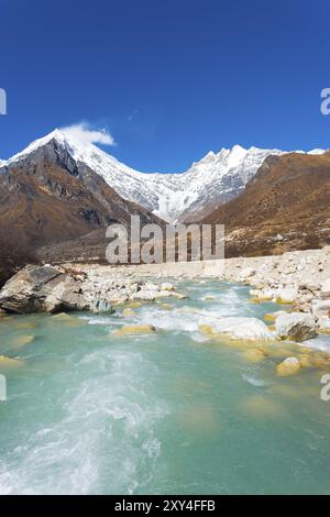 Ansicht des Langtang Lirung Peak, Teil des schneebedeckten Himalaya Gebirges hinter schnell fließenden Fluss der Gletscherwasser in großer Höhe in Nepal-Landschaft. Stockfoto
