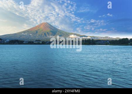 Der Fuji taucht in das Morgenlicht, während der Kawaguchiko-See an einem Sommertag in der fünf-Seen-Region Japans im Schatten unter dem bewölkten blauen Himmel liegt. Hor Stockfoto