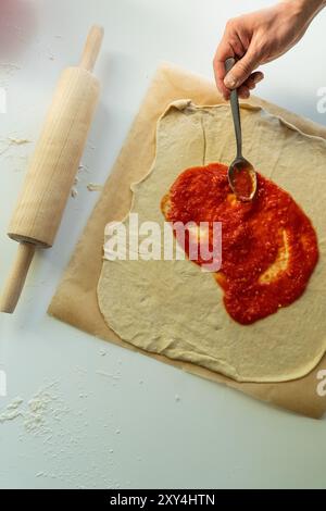Tomatensauce auf rohen Pizzateig verteilen Stockfoto