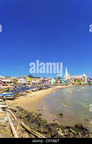 Kanyakumari, Indien, 22. Februar 2015: Die Kirche der Our Lady of Ransom Shrine hinter bunten Häusern an einem Sandstrand, der von Fischerbooten in Tamil Nadu besetzt ist Stockfoto