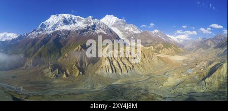 Großer Höhe geschwungenen Panorama der schneebedeckten Himalaya Annapurna Bergkette und Manang-Tal Dorf unten in Nepal Stockfoto