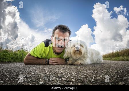 Ein Mann liegt mit seinem Hund auf der Straße und schaut in die Kamera Stockfoto