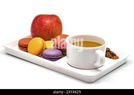 Bunte Macarons, Apfel, Mandeln und eine Tasse Kaffee auf einem weißen Tablett zum Frühstück Stockfoto