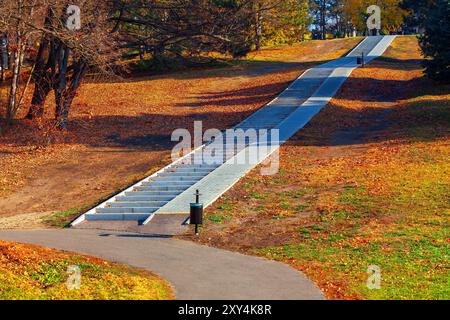 Pfad mit einer Treppe, die zu einem Hügel führt. Der Weg ist gesäumt von Bäumen und Herbstlaub Stockfoto
