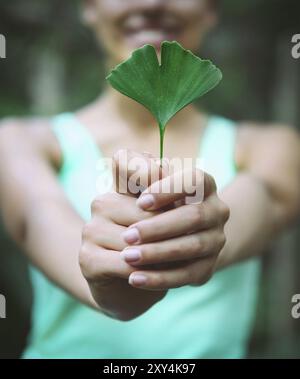 Lächelnde Frau Ginkgo Biloba Blatt in ihren Händen hält Stockfoto