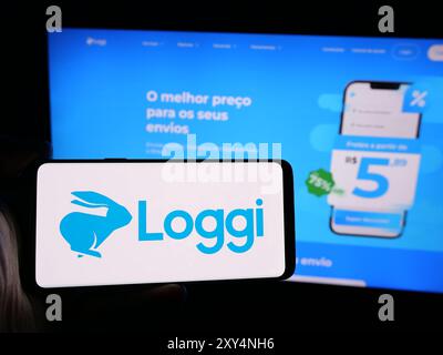 Person mit Smartphone mit Logo des brasilianischen Softwareunternehmens Loggi Tecnologia Ltda. Vor der Website. Schwerpunkt auf dem Display des Telefons. Stockfoto