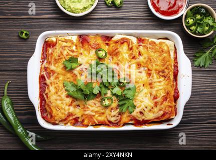 Traditionelles mexikanisches Gericht Enchiladas mit Fleisch, Chili-Soße und Käse in weißem Auflauf auf rustikalem Holzhintergrund, serviert mit Guacamole Stockfoto