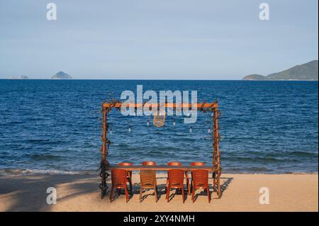 Verlassene Holztische und -Stühle am Sandstrand von Nha Trang vor dem Hintergrund des Meeres Stockfoto