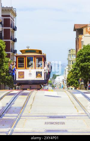 San Francisco, USA, 19. Mai 2016: Die entgegenkommende Seilbahn ist voll von draußen hängenden und plattformstehenden Touristen mit Bucht-Wasser-Hintergrund im sonnigen Powe Stockfoto