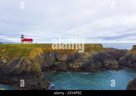 Fernsicht auf den felsigen Klippen oben Ocean Cove und dem historischen Point Cabrillo Licht Station Leuchtturm an einem bewölkten Abend in Mendocino, Kalifornien Stockfoto