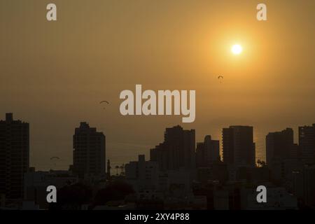 Foto von Gleitschirmfliegern bei Sonnenuntergang mit der Skyline des Viertels Miraflores in Lima, Peru, Südamerika Stockfoto