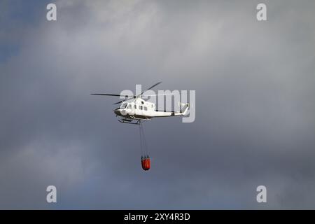 Die Brandbekämpfung Helikopter mit Bambi Korb mit Wasser auf dem Weg zu einem Brand geladen Stockfoto