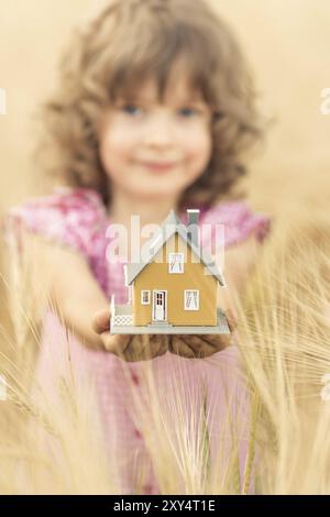 Glückliches Kind, das Haus in der Hand vor herbstgelbem Hintergrund hält. Immobilienkonzept Stockfoto